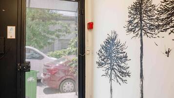 A hotel entrance with a black door, a green trash bin, and a wall mural of trees.