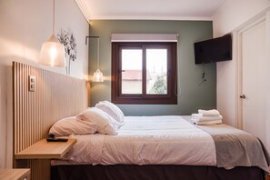 A bedroom with a bed, a bedside table, a lamp, a TV mounted on the wall, and a window with a view of buildings outside. - Style and Comfort in Providencia Ideal for 2 (Providencia)