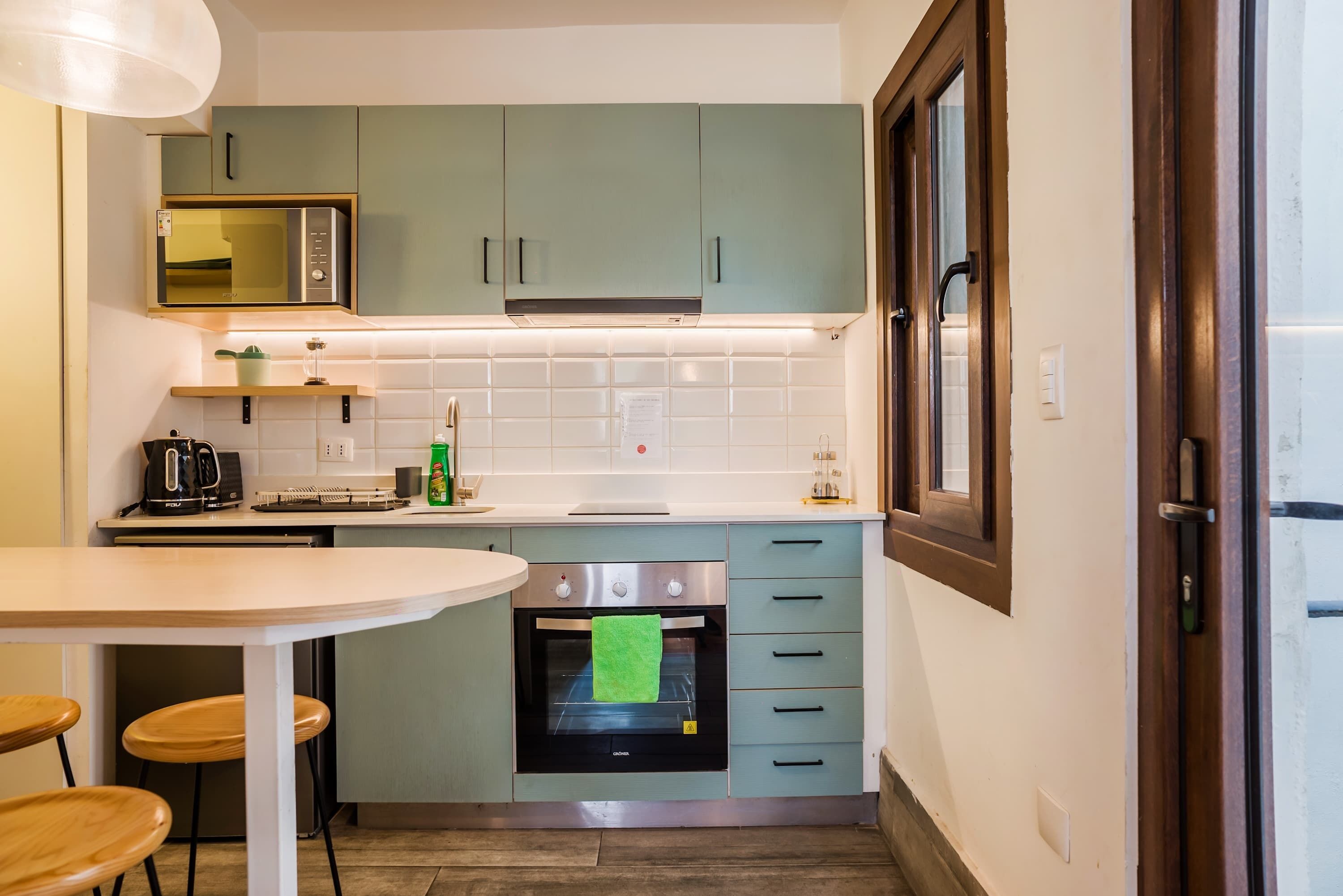 A compact kitchen with a microwave, stove, and a small oven. There is a dining table with chairs and a window with a view.