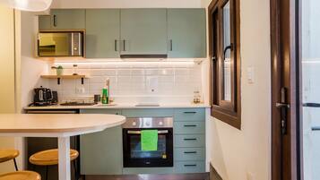 A compact kitchen with a microwave, stove, and a small oven. There is a dining table with chairs and a window with a view.