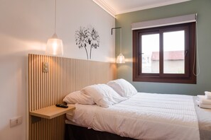 Ein Schlafzimmer mit einem hölzernen Kopfteil, einem Bett mit weißer Bettwäsche, einem Nachttisch mit Fernbedienung und einem Fenster mit Blick auf Gebäude.