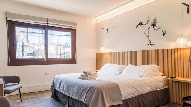 Ett hotellrum med en säng, ett skrivbord, en stol, ett fönster och en vägglampa.
