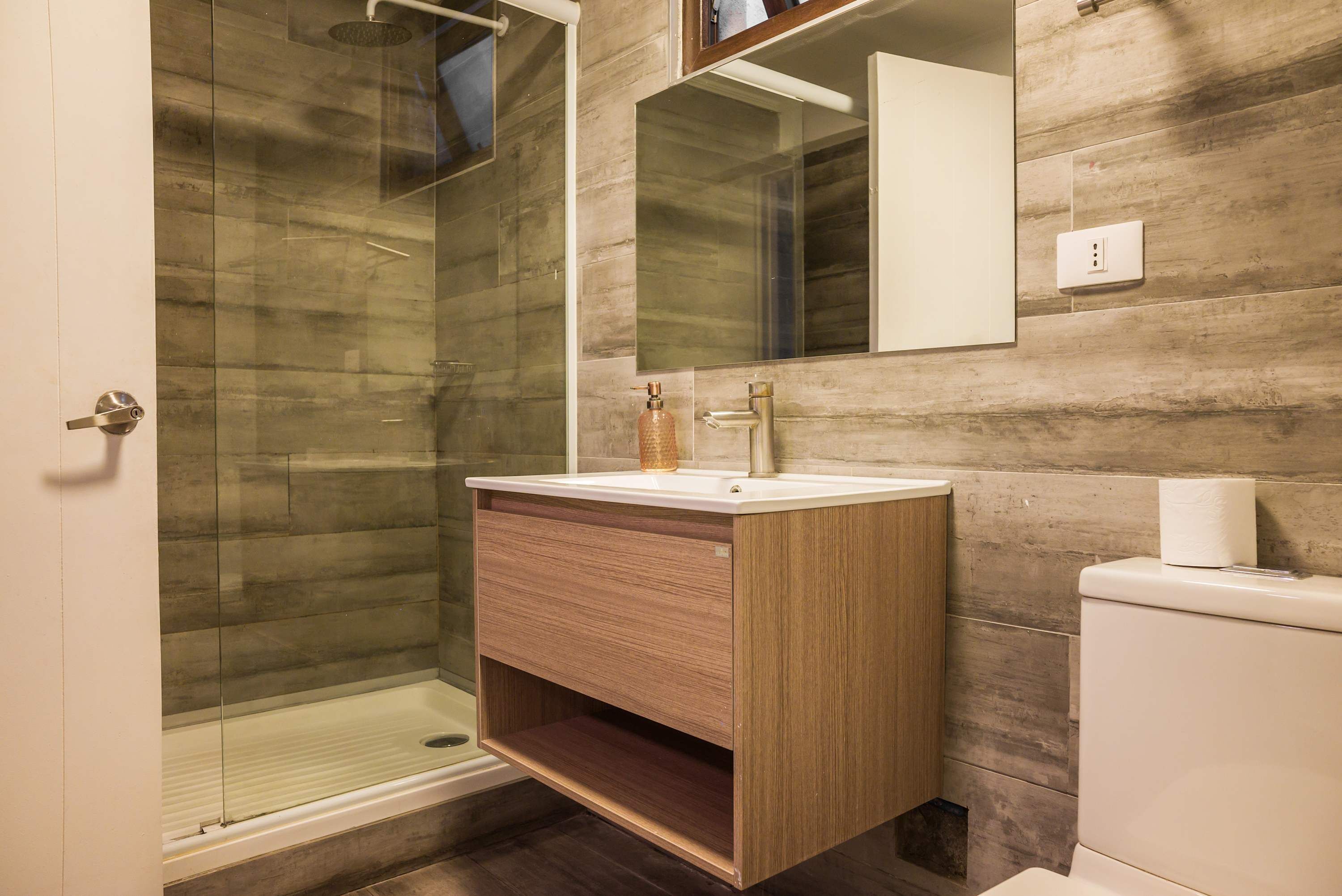 A modern bathroom with a glass shower enclosure, a wooden vanity, and a white toilet.