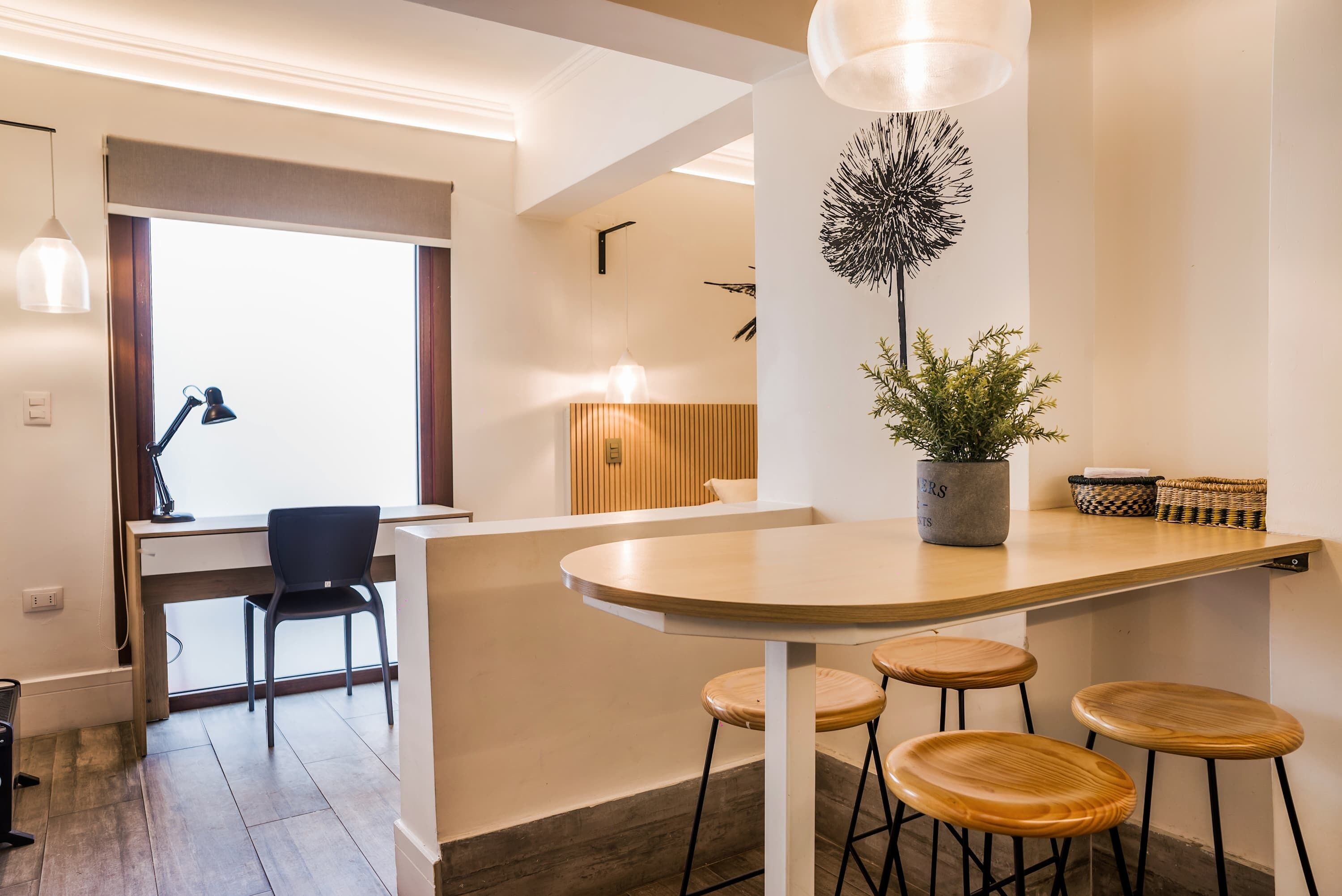 A modern kitchen with a wooden island, bar stools, a potted plant, and a dining area with a chair and table.