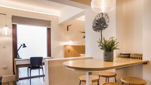 Een moderne keuken met een houten kookeiland, barkrukken, een potplant en een eethoek met een stoel en tafel.