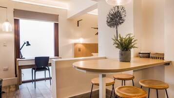 A modern kitchen with a wooden island, bar stools, a potted plant, and a dining area with a chair and table.