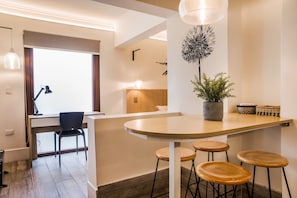 A modern kitchen with a wooden island, bar stools, a potted plant, and a dining area with a chair and table.