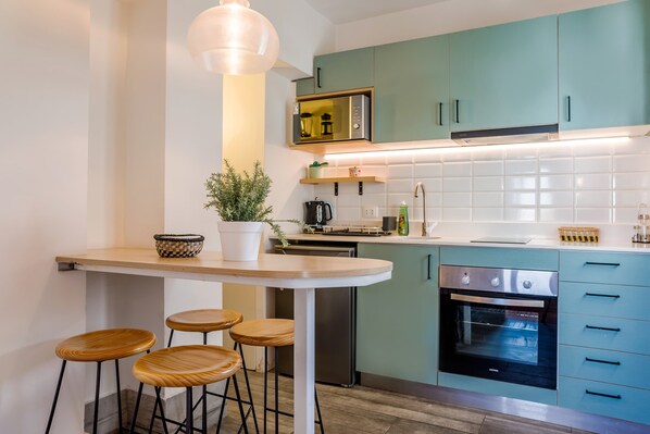 Una cucina moderna con mobili color petrolio, un piano di lavoro bianco, forno integrato, microonde e una pianta in vaso.