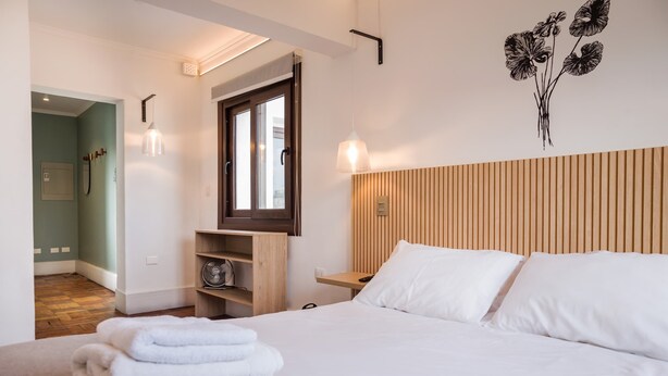 Habitació d'hotel amb llit, capçalera de fusta, finestra, llum penjada a la paret i una obra d'art mural.