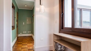 Passadís amb sòl de fusta, finestra amb marc fosc, lluminària fixada a la paret i un ventilador sobre una estant.