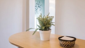Zona de menjador amb taula de fusta, dues cadires, llum penjant, una planta en test i cistella teixida.