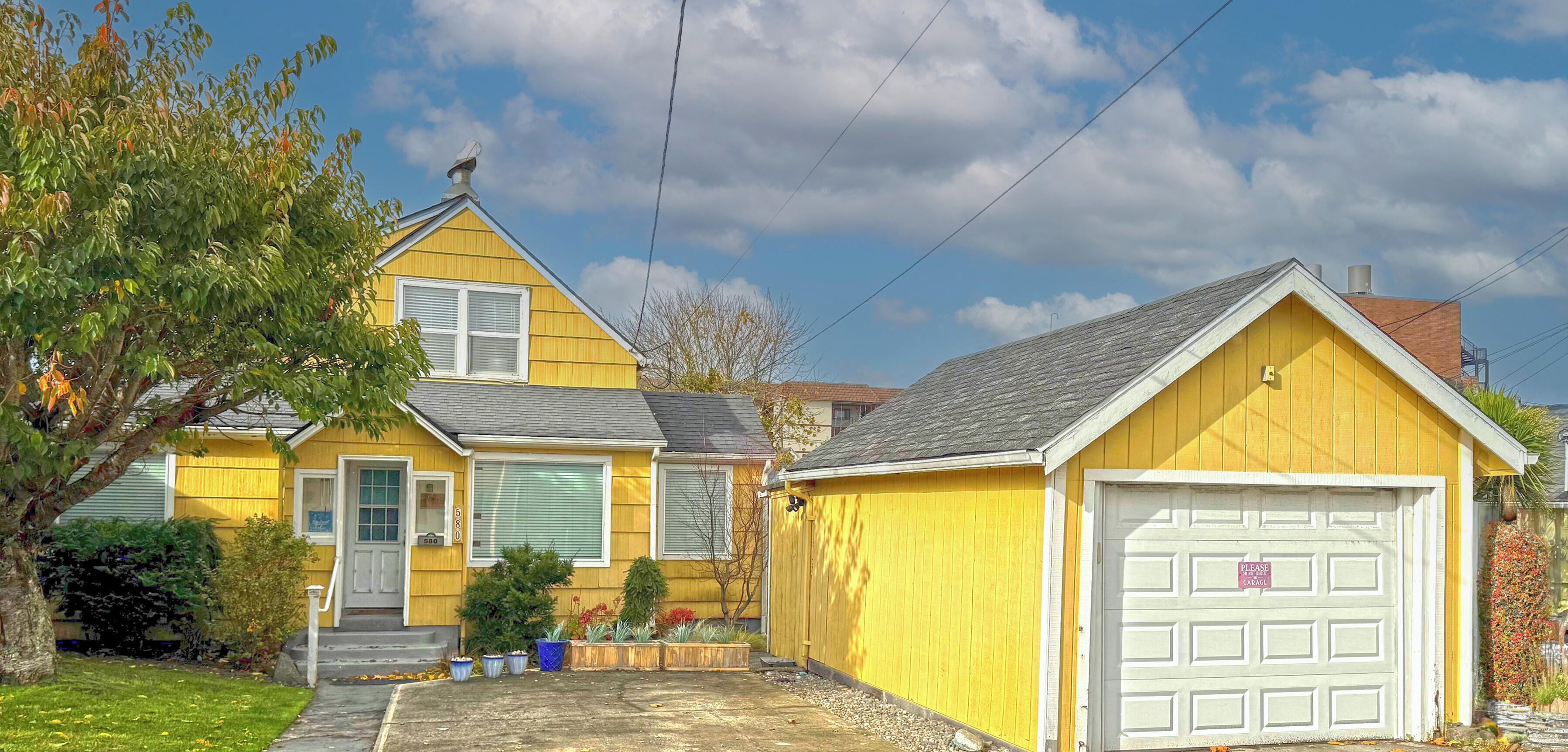 A yellow house with a garage, a front porch, and a small garden.