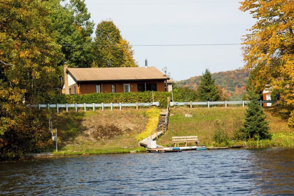 Une maison au bord d’un lac, avec un quai et un escalier en bois menant à ce quai.