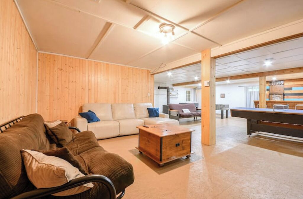 Un grand salon avec un mur en bois, un canapé, une table basse et une table de billard.