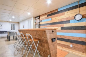 A bar area with a wooden wall, bar stools, and a clock.