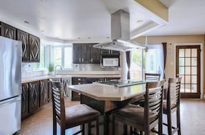 A modern kitchen with dark cabinetry, a stainless steel refrigerator, a microwave, and a large island with bar stools.