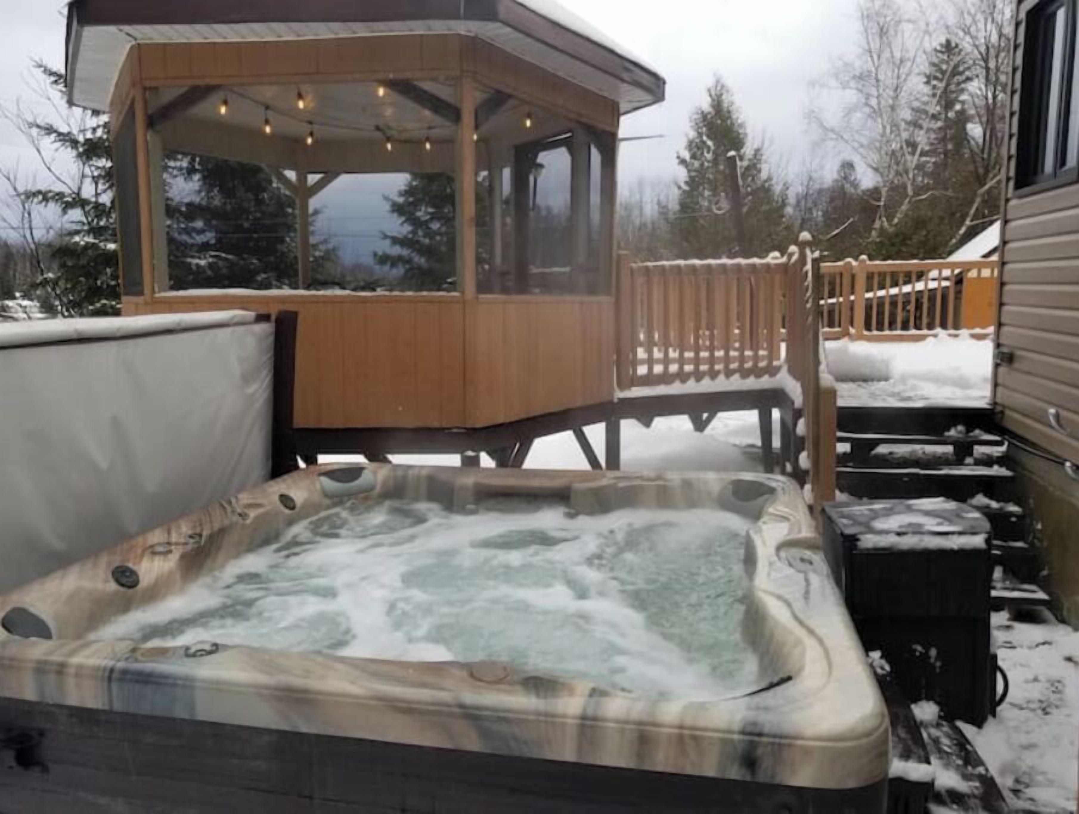 Un bain à remous avec une terrasse en bois et un espace salon couvert.