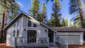 A two-story house with a covered porch, a garage, and a forested backdrop. - Oglala Little Lodge - Cabin Getaway (South Lake Tahoe)