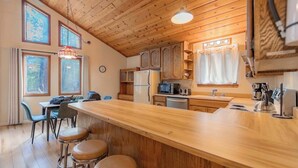 A kitchen with wooden cabinets, a refrigerator, a microwave, a sink, and a bar area with stools. - Oglala Little Lodge - Cabin Getaway (South Lake Tahoe)