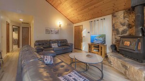A living room with a leather sofa, a round coffee table, a stone fireplace, and a television. - Oglala Little Lodge - Cabin Getaway (South Lake Tahoe)