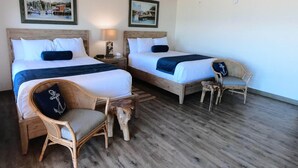 A room with two beds, a chair, a small table, and a lamp. There are two framed pictures on the wall. - Island Suites - Beachfront, boutique hotel, walk to lighthouse, dining & more (St George Island)