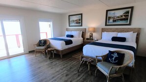 Een hotelkamer met twee bedden, een houten vloer en uitzicht door een groot raam.