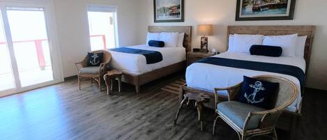 A hotel room with two beds, a wooden floor, and a view through a large window.
