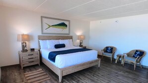 A bedroom with a wooden bed, two bedside tables, a nightstand, a chair, and a wall-mounted painting. - Island Suites - Beachfront, boutique hotel, walk to lighthouse, dining & more (St George Island)
