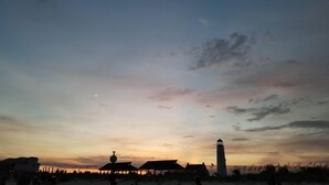 A coastal scene with a lighthouse, beach huts, and a clear sky. - Island Suites - Beachfront, boutique hotel, walk to lighthouse, dining & more (St George Island)