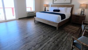 A spacious bedroom with a large bed, a wooden floor, and a view through a sliding glass door. - Island Suites - Beachfront, boutique hotel, walk to lighthouse, dining & more (St George Island)