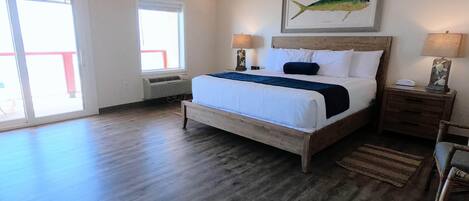 A spacious bedroom with a large bed, a wooden floor, and a view through a sliding glass door.