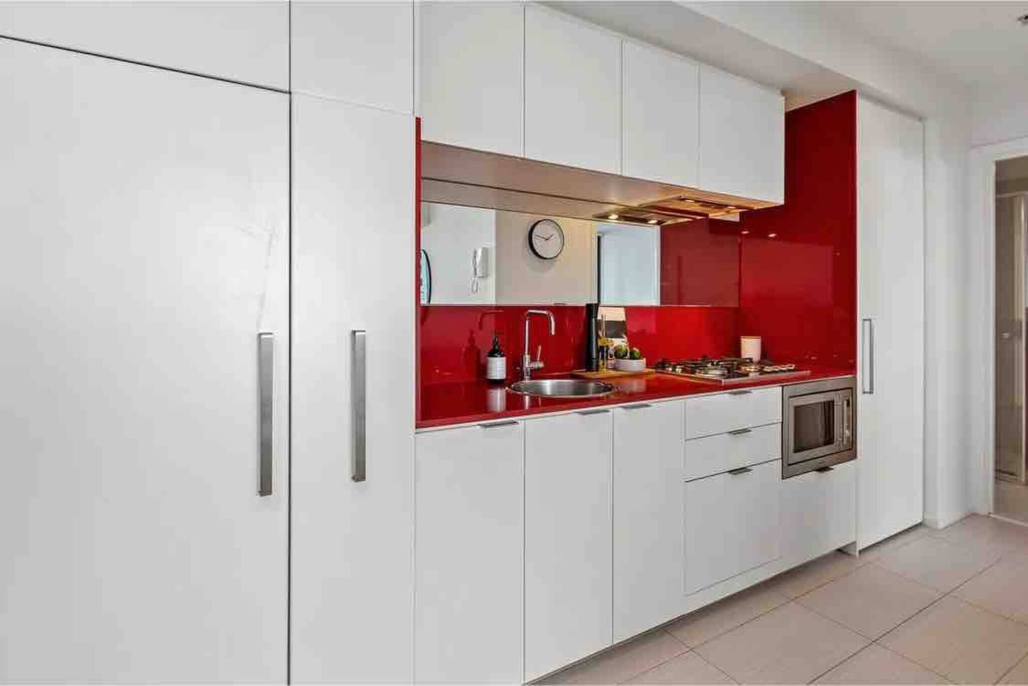 A modern kitchen with white cabinets, a red countertop, a microwave, and a clock on the wall.
