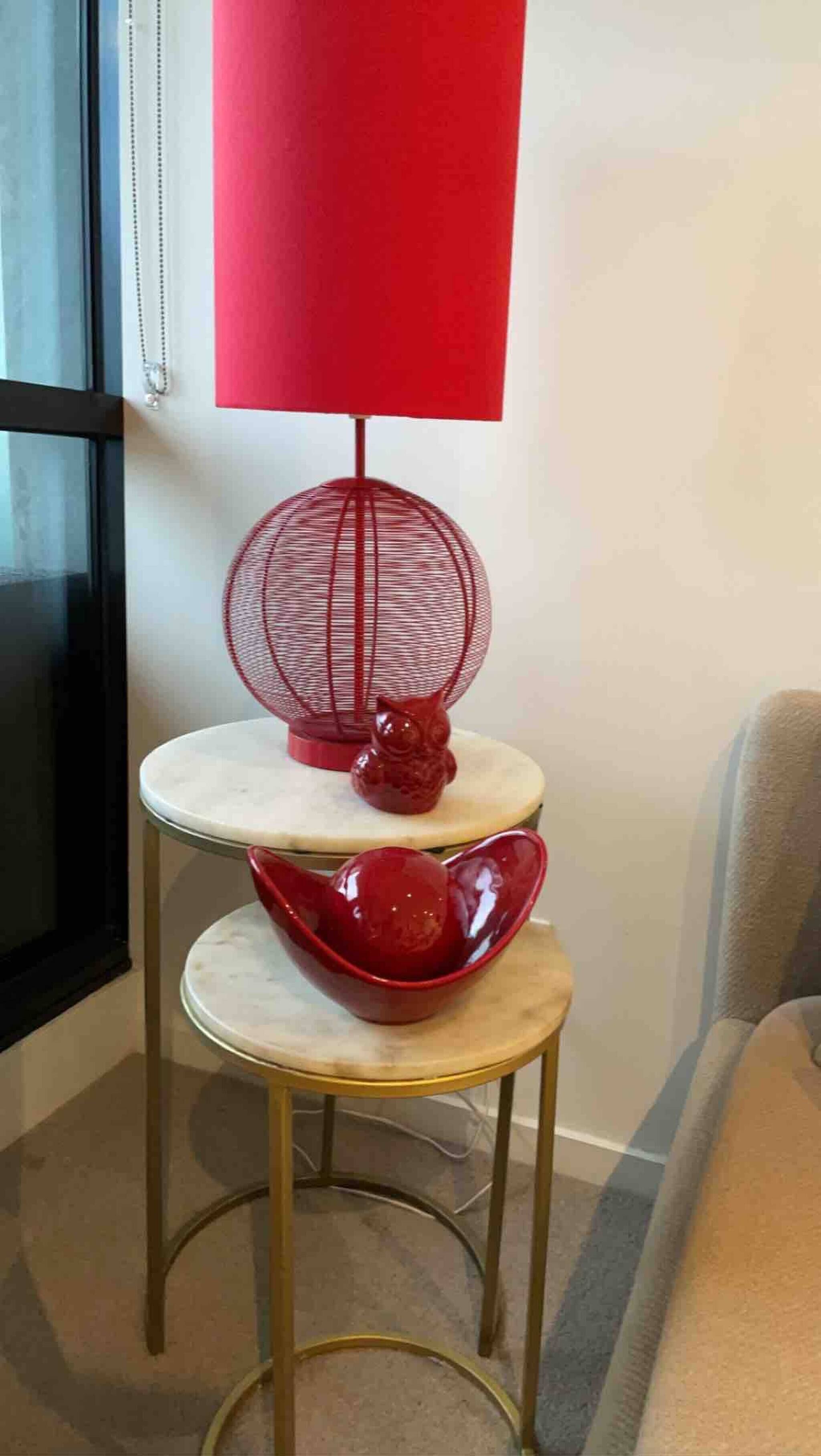 Ett bord i tre våningar med en röd lampa, ett rött, sfäriskt föremål och en röd ugglefigur.