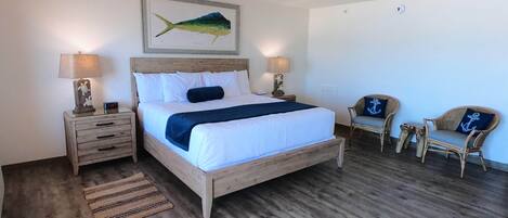 A bedroom with a wooden bed, two bedside tables, a nightstand, a chair, and a wall-mounted painting.