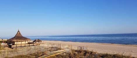 A beach with a wooden fence, a thatched-roof building, and a clear blue sky.