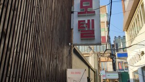 A narrow street with buildings on either side, a sign for a store, and a CCTV security sign. - Sopung Motel  (Seoul)