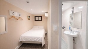 Habitación de hotel con cama, mesita de noche, espejo en la pared y baño con lavabo y ducha.
