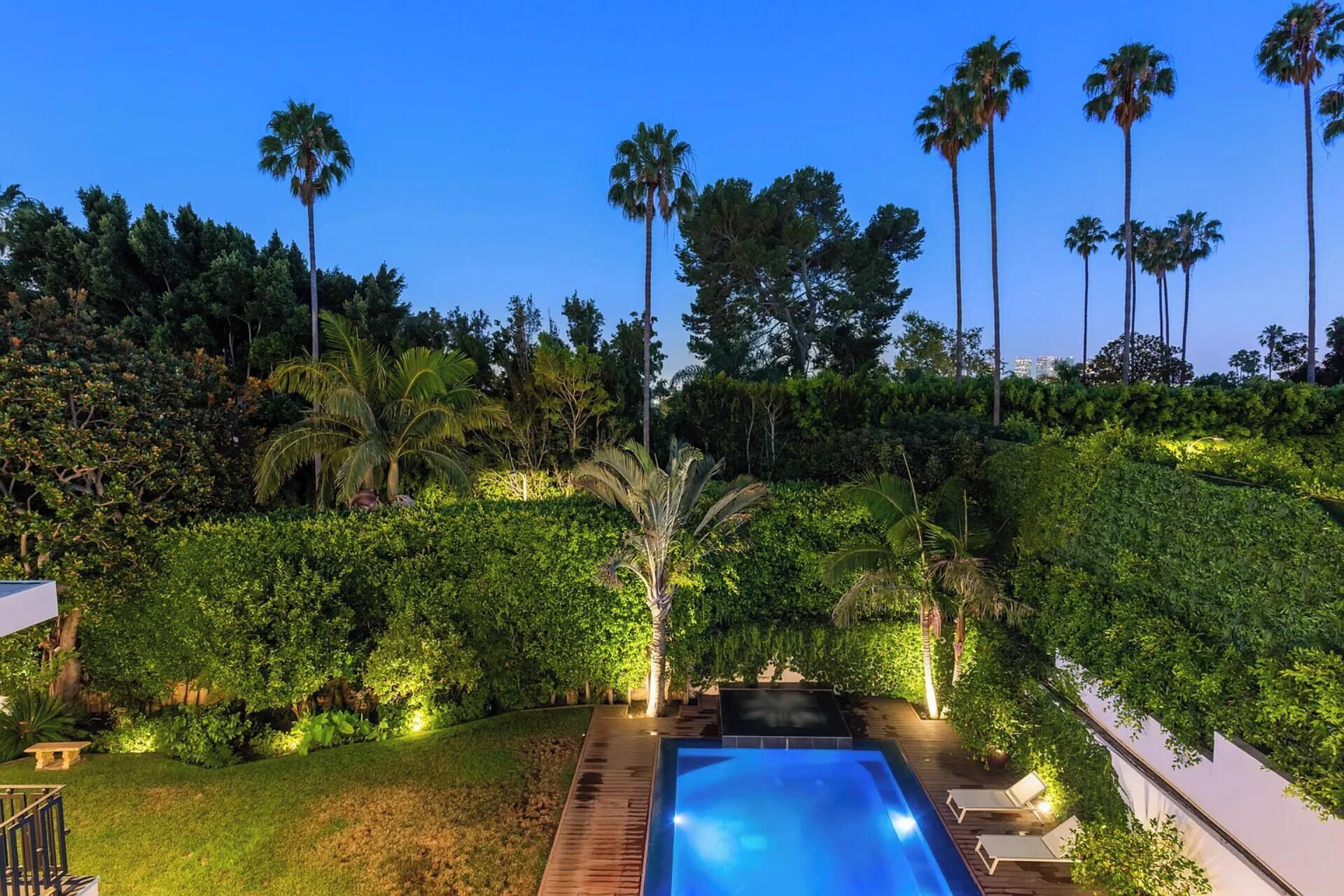 A swimming pool with lounge chairs, surrounded by lush greenery and tall palm trees.