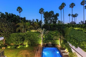 A swimming pool with lounge chairs, surrounded by lush greenery and tall palm trees. - Alta Royale - Exquisite Designer Retreat Near Soho House & Rodeo Drive (West Hollywood)
