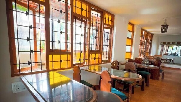 A traditional-style room with wooden furniture, large windows with decorative grilles, and a tiled floor.