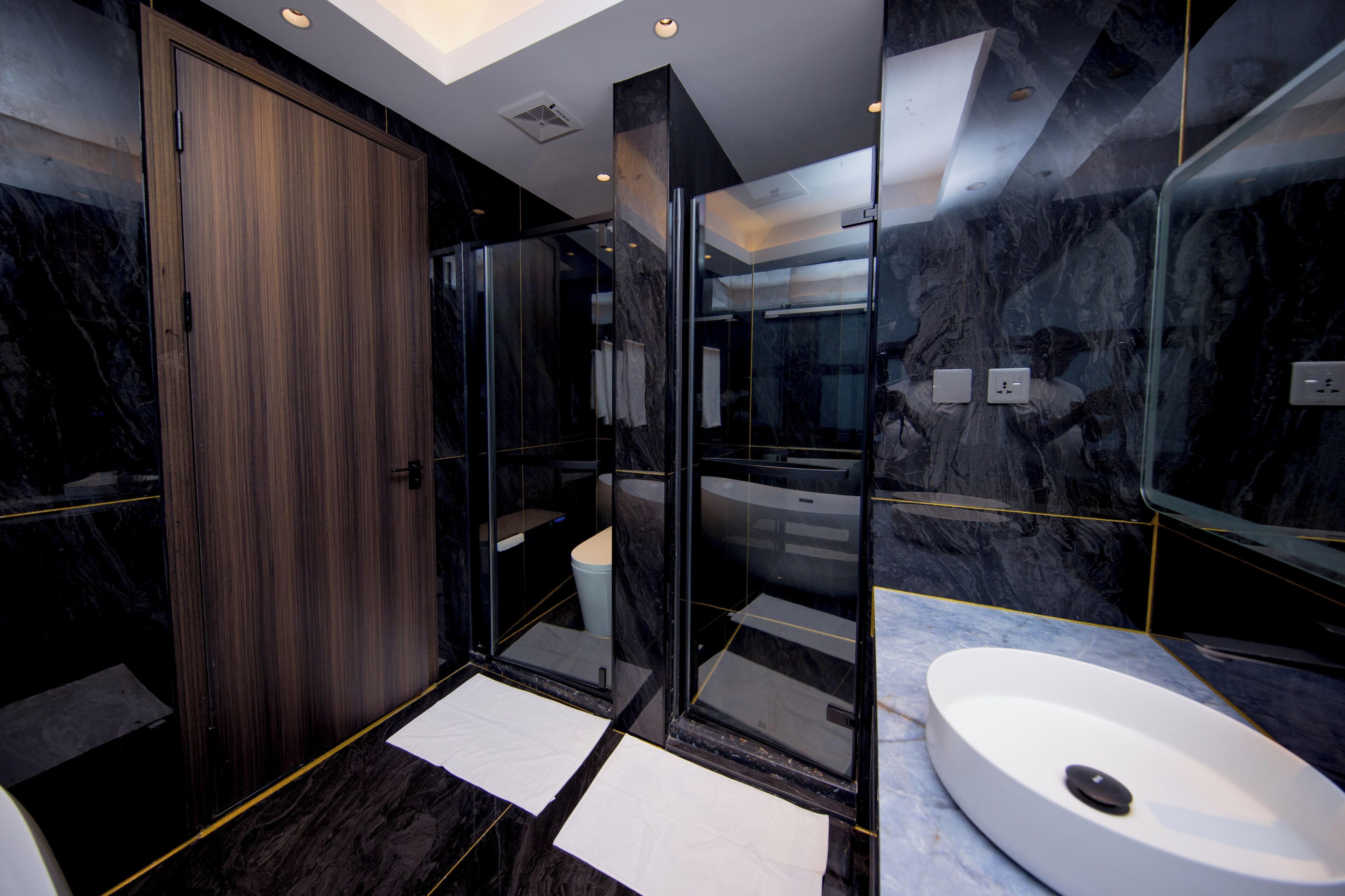 Un bany modern amb una porta de fusta, una cabina de dutxa de vidre i un lavabo blanc.