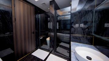Un bany modern amb una porta de fusta, una cabina de dutxa de vidre i un lavabo blanc.