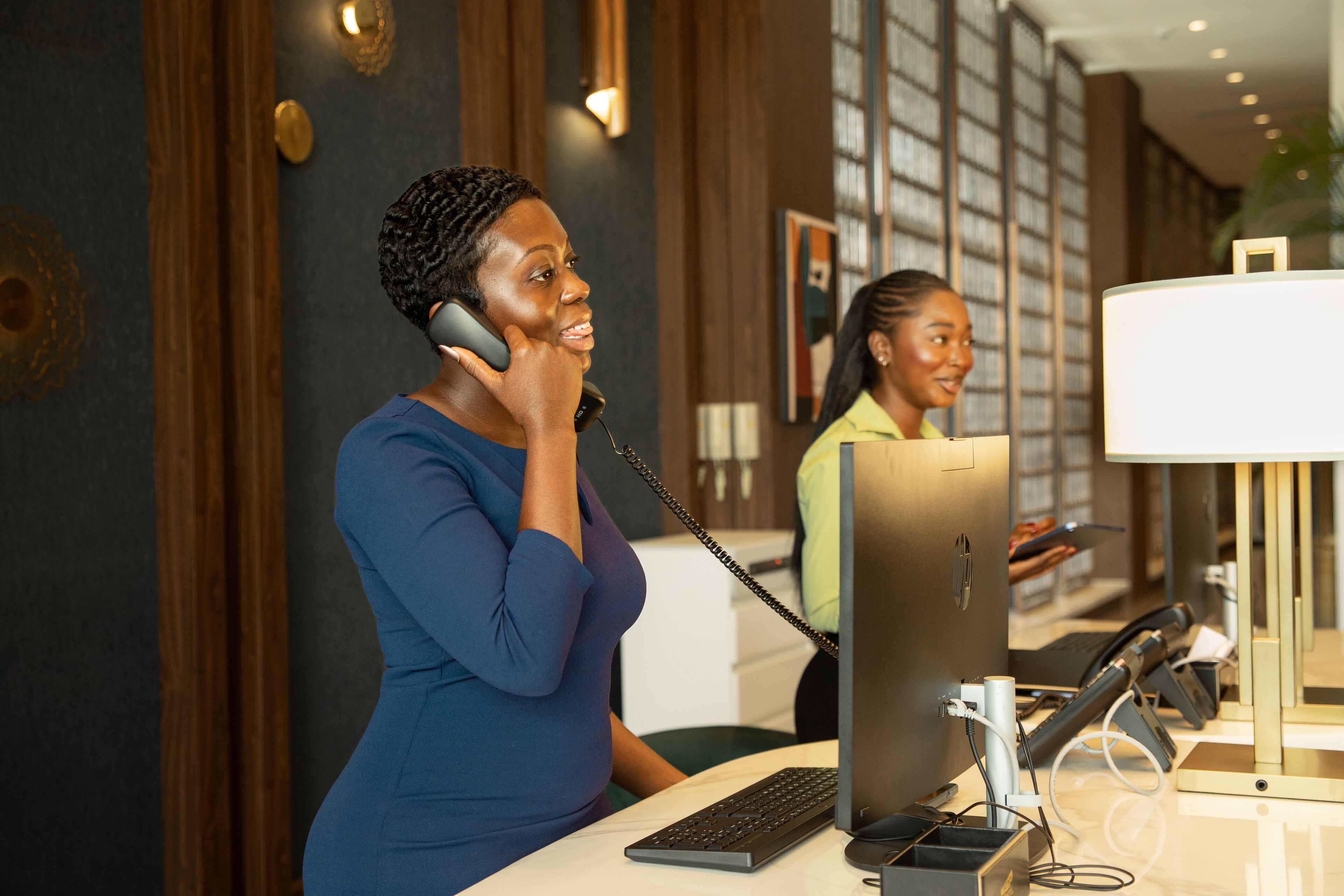 A reception desk with a computer and telephone, a lamp, and a framed picture on the wall.