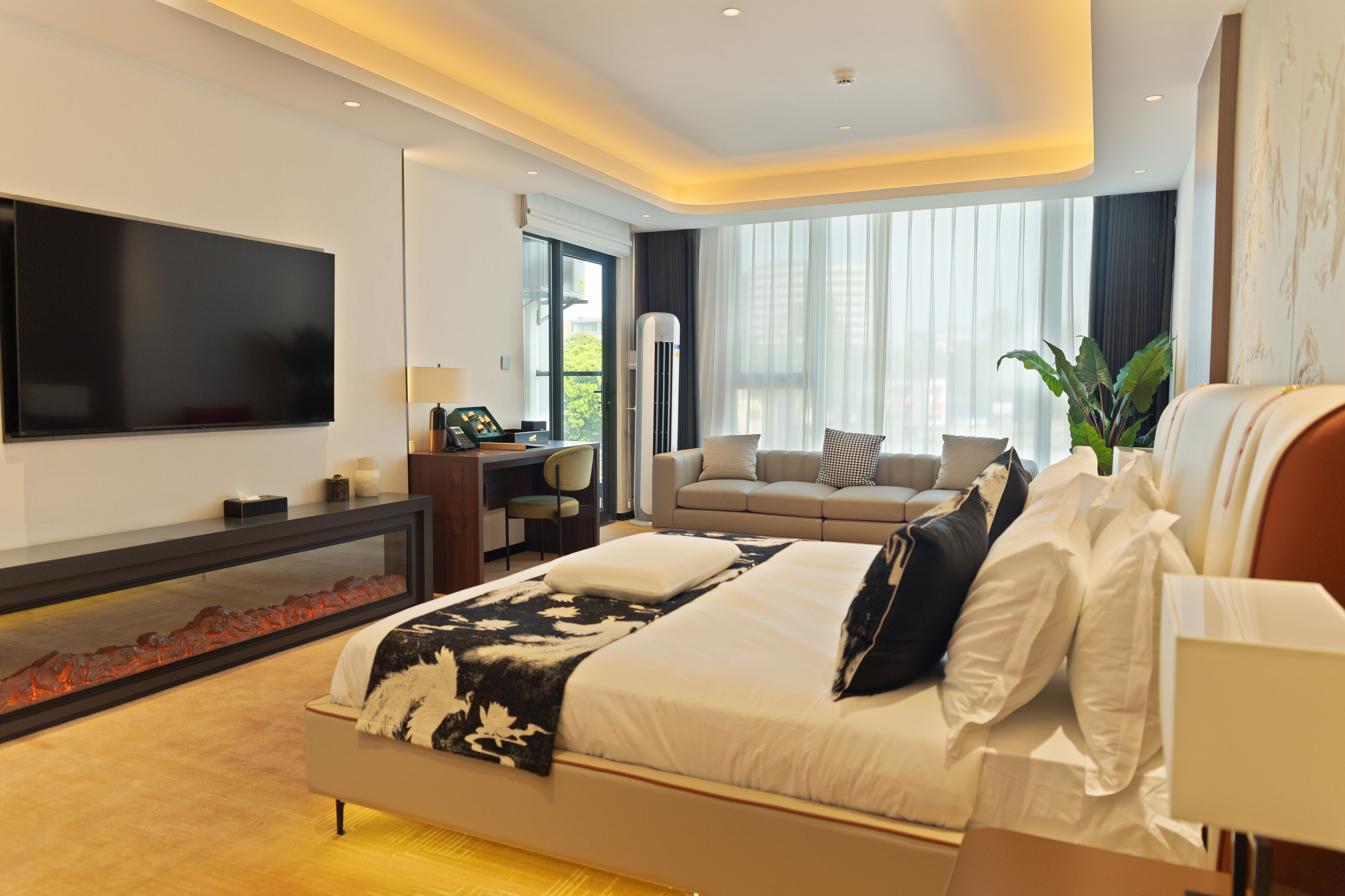 A modern hotel room with a large bed, a desk, a sofa, and a TV.