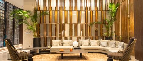 A modern living room with a curved sofa, two armchairs, a coffee table, and decorative plants.