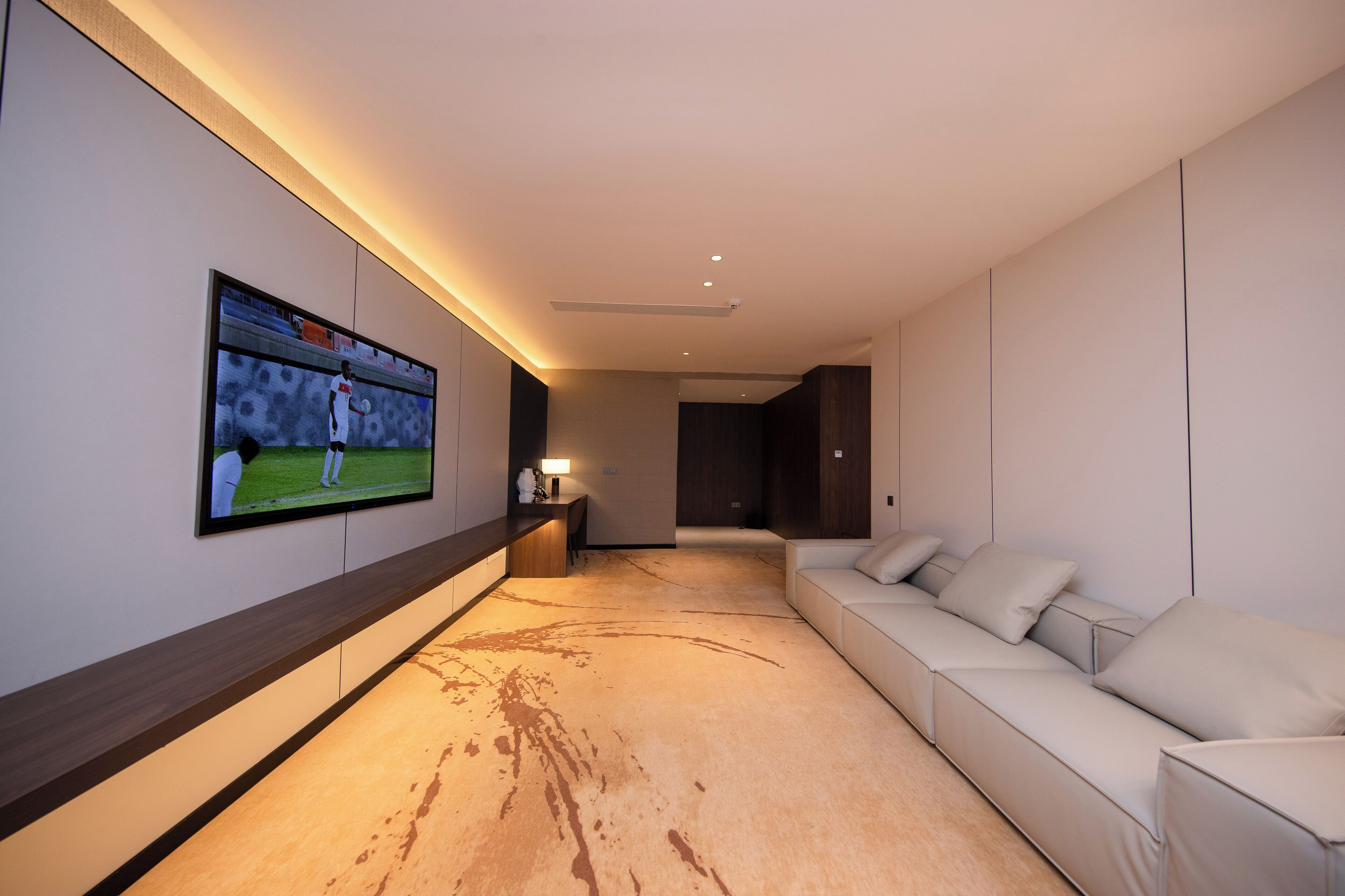 A modern living room with a large flat-screen TV mounted on the wall, a beige sofa, and a wooden floor with a stain.