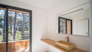 A modern bathroom with a wooden vanity, a large mirror, and a view of trees through a sliding door. - Villa Benedettu (Lecci)