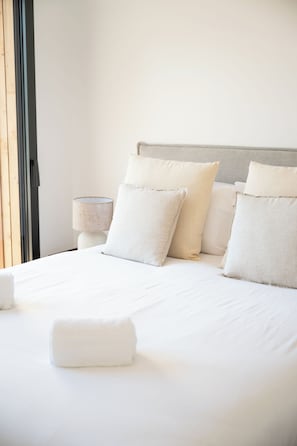 A neatly made bed with pillows and a rolled towel, a bedside lamp, and a window with a view. - Villa Benedettu (Lecci)