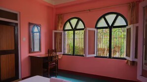 Une pièce aux murs roses, avec un lit, un bureau et deux fenêtres grillagées.