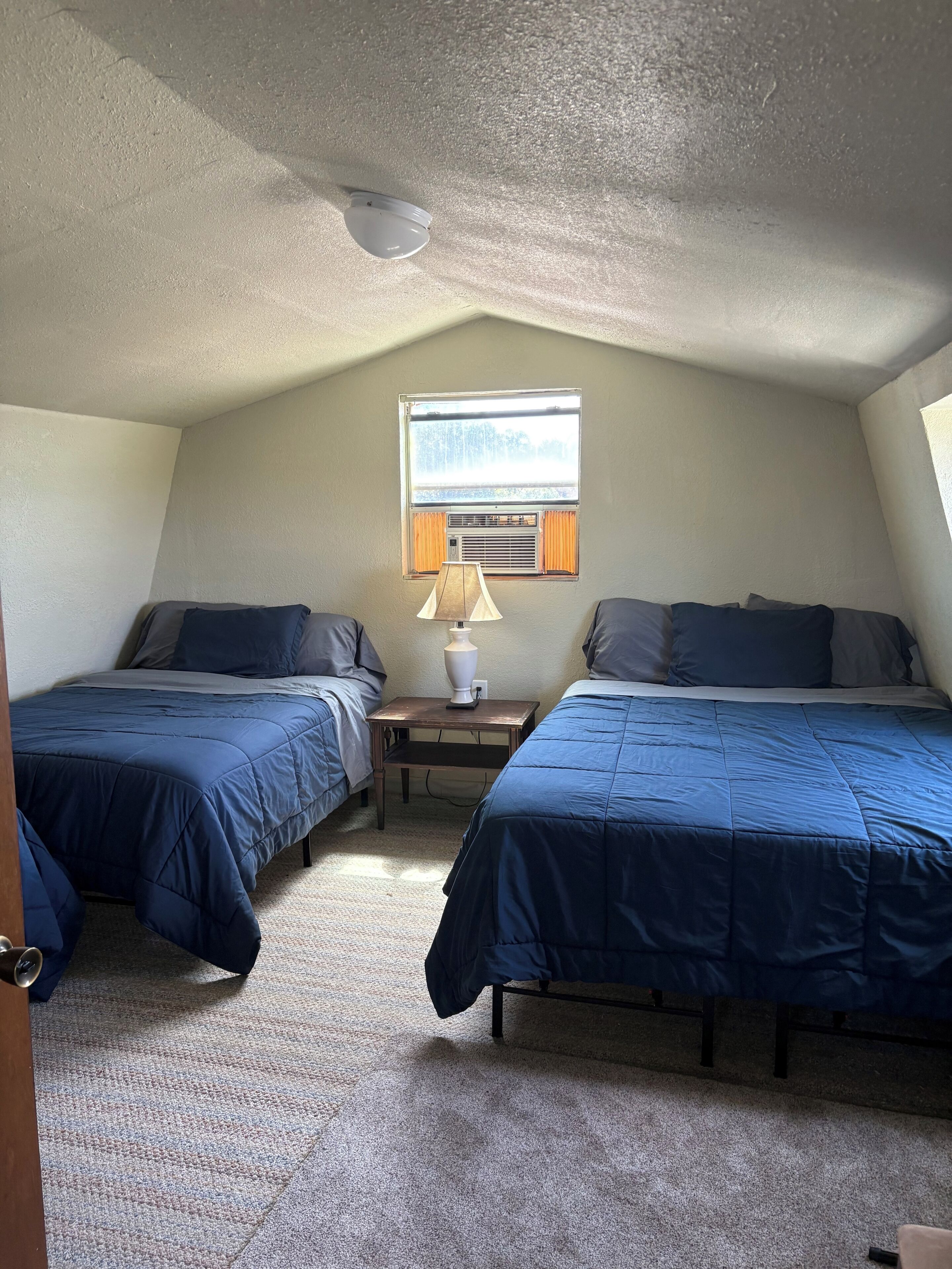 Ein Zimmer mit zwei Betten, einem Fenster, einer Lampe und einem Deckenventilator.